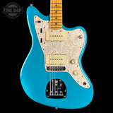 A turquoise blue electric guitar with a cream paisley patterned pickguard, cream humbucker pickups, and a maple neck, shown against a solid black background.