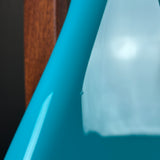 Close-up of a glossy turquoise blue curved object, possibly a chair or table component, with a white surface and a dark brown wooden vertical element in the background.