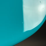 Close-up of a glossy turquoise-blue curved surface with a bright white highlight and a dark shadow along the edge.