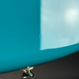 Close-up of a glossy turquoise-blue curved surface, likely part of a bathtub or similar vessel, with a small metallic drain visible at the bottom against a dark background.
