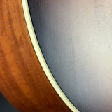 Close-up detail of a guitar body showing the warm brown wood edge, a cream binding strip, and the dark gray to black backplate.
