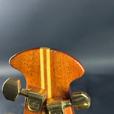 Close-up of a guitar's wooden headstock with tuning pegs against a dark background