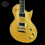 A gold-finish electric guitar with a cutaway body, black pickups, chrome hardware, and a dark fretboard, shown against a solid black background with a Tone Shop watermark in the top left.