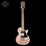 A pinkish-rose gold electric guitar with a black pickguard and chrome hardware, shown against a solid black background. A Tone Shop watermark is visible in the top-left corner.