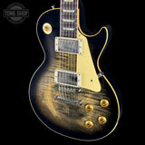 Electric guitar with a black and gold finish on a black background, featuring the Tone Shop logo.