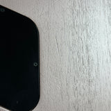 A close-up of a black electronic device corner with a screw on a textured light gray surface.