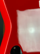Close-up of a red guitar with a clear plastic cover on the neck