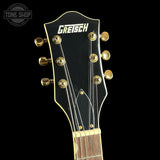 Close-up of a Gretsch acoustic guitar headstock with gold tuning pegs and white Gretsch branding on a black background.