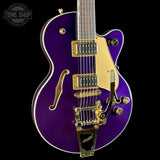 A purple electric guitar with gold hardware and trim, shown from a front-facing angle against a black background. A Tone Shop watermark is visible in the top-left corner.