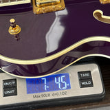 Close-up of a purple electric guitar body resting on a digital scale displaying 7.45 lbs, with gold hardware and cream trim visible.