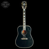A black acoustic guitar with gold hardware and white binding, shown vertically against a solid black background. A Tone Shop watermark is visible in the top-left corner.