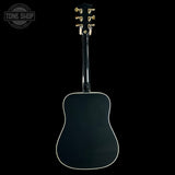 The back of a black acoustic guitar with gold tuning keys and white edge trim, shown against a solid black background with a Tone Shop watermark in the top left corner.