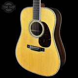 A close-up studio shot of a wooden acoustic guitar against a solid black background, featuring a natural wood finish on the front and a dark brown side, with a Tone Shop watermark in the upper left corner.