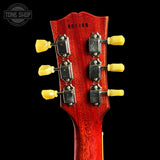 Close-up of the headstock of a red electric guitar against a black background, showing six yellow tuning pegs and a Tone Shop watermark in the top left corner.