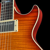 Close-up of an electric guitar body showing a sunburst orange wood finish, white binding, and part of the dark fretboard against a black background.