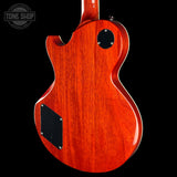 The back of an electric guitar with a glossy reddish-orange sunburst finish, featuring a black pickguard and circular control plate, shown against a black background with a Tone Shop watermark.