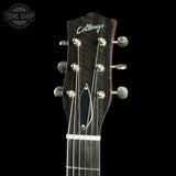 Close-up of the headstock of a Collings acoustic guitar against a black background, showing the brand name in white script, six silver tuning pegs, and part of the dark wood fretboard with white fretboard lines.
