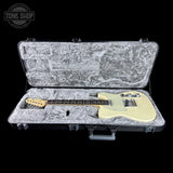 An electric guitar with a cream-colored body and maple neck, displayed inside an open gray hard case on a solid black background. A Tone Shop logo is visible in the top-left corner.