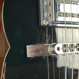 Close-up of a black electric guitar body showing the bridge, tremolo arm, pickups, and strings, with visible scratches on the glossy finish.