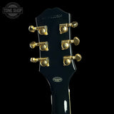 Close-up rear view of a guitar headstock in glossy black with gold tuning pegs, shown against a black background. The headstock has a scalloped top edge and visible 'Zellweg' branding at the top.