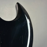 Close-up of a glossy black guitar body edge with visible scratches and a white reflection, set against a plain light gray background.