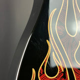Close-up of a glossy black guitar body featuring a red and gold flame and paisley graphic design.