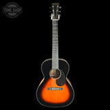 A Martin acoustic guitar with a classic sunburst finish, featuring a bright orange center and a dark black outer edge, shown against a solid black background with a Tone Shop watermark in the top left corner.