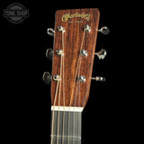 Close-up of the headstock of a Martin & Co. acoustic guitar, showing the dark brown wood grain, gold script logo, and six tuning pegs against a solid black background.