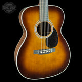 A classic acoustic guitar with a sunburst finish, featuring a warm amber-brown center fading to dark brown edges, set against a solid black background.