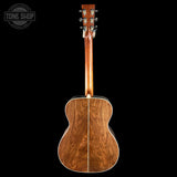 The back view of a wooden acoustic guitar with a rich brown wood finish and silver tuning keys, shown against a solid black background with a Tone Shop watermark in the top left corner.