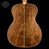 Close-up of the back of an acoustic guitar showing a rich, symmetrical wood grain pattern in warm brown tones, with a white binding edge against a solid black background.