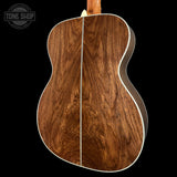 Close-up of the back of an acoustic guitar showing a rich, dark brown wood grain finish with a white binding edge, set against a solid black background.