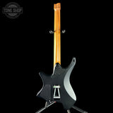 Black electric guitar with a wooden neck on a black background, featuring 'Tone Shop' branding.