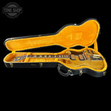 An electric guitar with a black body and gold maple interior, displayed inside an open black hard case with a gold velvet lining against a black background. A Tone Shop watermark is visible in the top left corner.