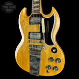 A Gibson SG electric guitar with a natural wood finish, featuring a black pickguard, dual humbucker pickups, and a chrome tailpiece, shown against a solid black background.