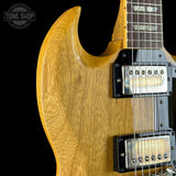 Close-up of a natural wood electric guitar body with black hardware and dual humbucker pickups, shown against a black background with a Tone Shop watermark in the top left.