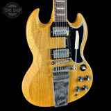 A Gibson SG electric guitar with a natural wood finish, black pickguard, and chrome hardware, shown against a solid black background with a Tone Shop watermark in the top left corner.