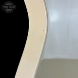 Close-up of a curved cream-colored object, likely a guitar body or similar wooden instrument edge, showing minor scuffs and wear, with a black background on the left and a light gray reflective surface on the right.