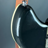 Close-up of a black guitar headstock with a silver tuning peg on a gray background