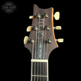 Close-up of the headstock of a McCarty S94 acoustic guitar against a black background, featuring a dark wood finish, cream tuning pegs, and a white signature on the headstock.