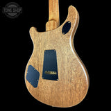 The back of an electric guitar with a natural wood finish and black pickguard plates, shown against a solid black background with a Tone Shop watermark in the top left corner.