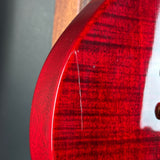 Close-up of a glossy red guitar body showing the flamed wood grain and a visible vertical scratch on the finish.