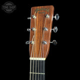 Close-up of the headstock of a Martin & Co acoustic guitar, showing the brown wood grain, six silver tuning pegs, and six strings, set against a solid black background with a Tone Shop watermark in the top left corner.