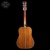The back of a wooden acoustic guitar with a glossy mahogany-style finish, shown against a solid black background. A Tone Shop watermark is visible in the top-left corner.