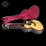 An acoustic guitar with a natural wood body and black pickguard displayed inside an open hard case with a bright pink velvet interior, set against a solid black background.