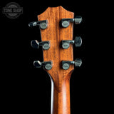 Close-up of the headstock of an acoustic guitar, showing six tuning pegs with Taylor logos and a warm brown wood finish against a black background.