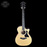 A Taylor acoustic-electric guitar with a natural wood finish and black pickguard, shown against a solid black background with a Tone Shop watermark in the top-left corner.