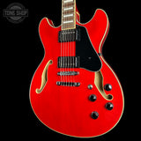 A red electric guitar with a black pickguard and gold-toned hardware, shown against a black background with a Tone Shop watermark in the top left corner.