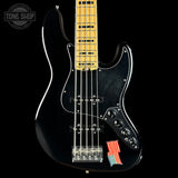 A black electric bass guitar with a maple neck, chrome hardware, and a small American flag sticker on the lower bout, shown against a black background with a Tone Shop logo in the top left corner.