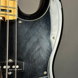 Close-up of a black electric bass guitar body with a chrome pickguard, silver hardware, and part of the gold-toned neck and strings.
